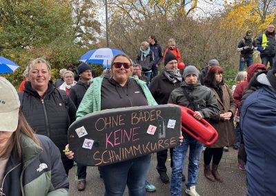 Demonstrierende mit einem Schwimmbrett mit der Aufschrift „Ohne Bäder keine Schwimmkurse“ und einer roten Rettungsboje.