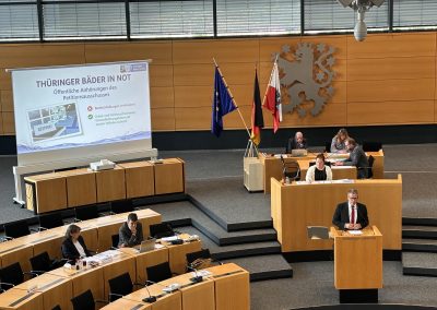 Redner am Pult des Thüringer Landtags neben einer Präsentation zum Erhalt der Bäder und ihrer Schwimm- und Gesundheitsangebote.